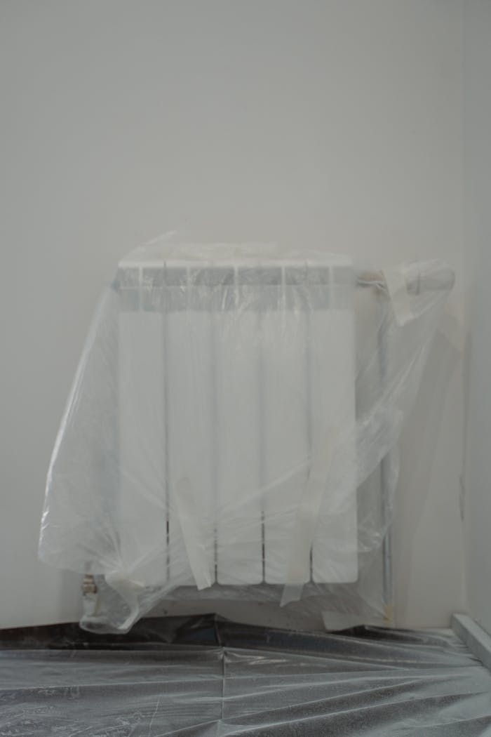 A radiator protected by plastic wrap, indoors, prepared for renovation.